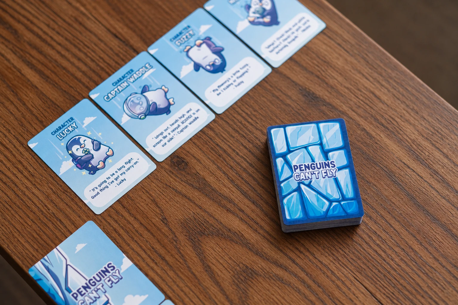 Penguins Can’t Fly character cards and a blue card deck arranged on a wooden table